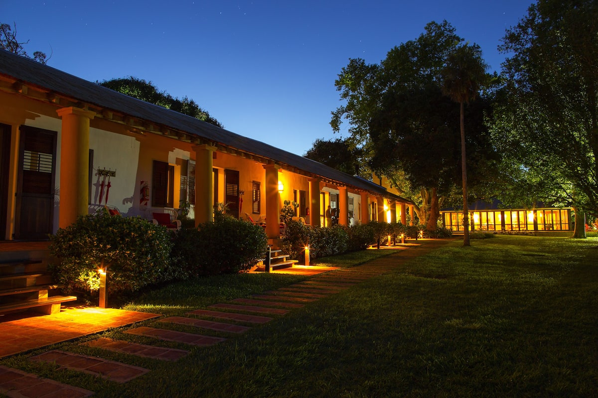 A hotel with a row of rooms, a well-lit pathway, and a garden area.