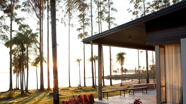 A modern building with a covered outdoor area, a bench, and a view of a body of water and trees.
