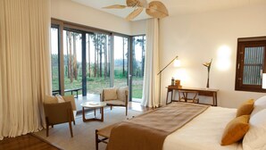 A modern bedroom with a large bed, a desk, and a view of the outdoors.