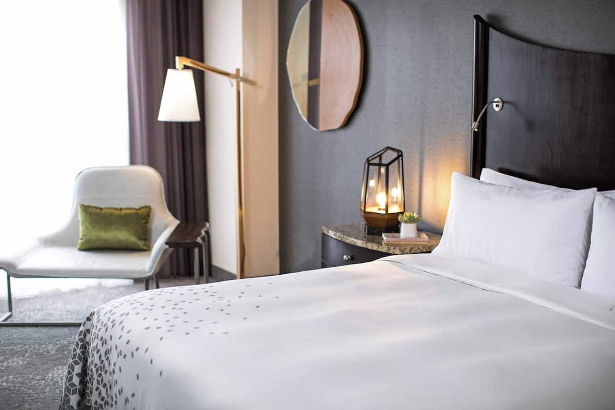 Une chambre d’hôtel avec un grand lit, une chaise, une table de chevet avec une lampe et un miroir fixé au mur.