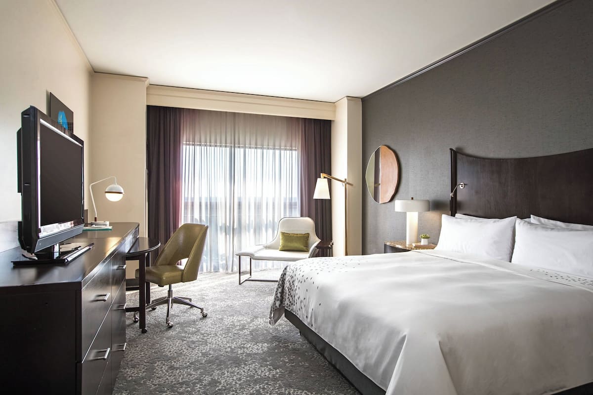 Une chambre d’hôtel avec un grand lit, un bureau avec une télévision, une chaise et une fenêtre avec des rideaux.