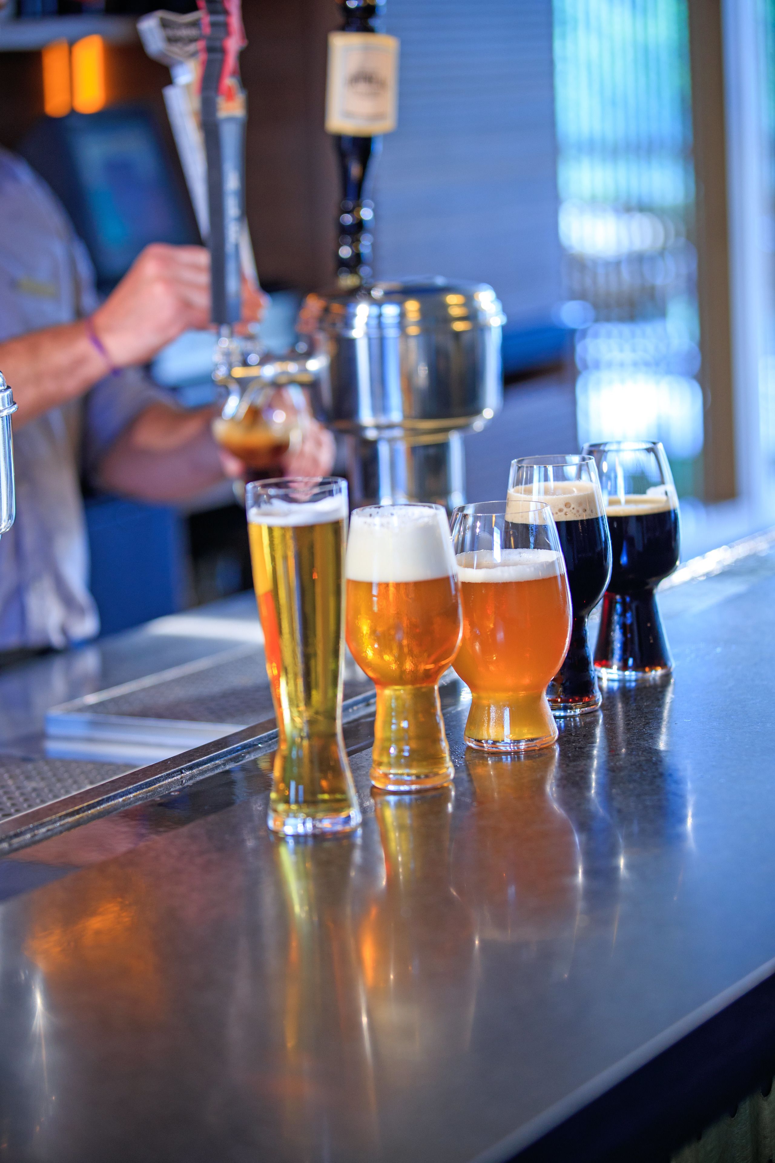 A bar counter with several glasses of beer and a beer tap.
