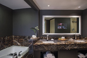 A modern bathroom with a dark marble countertop, a large mirror, a bathtub, and neatly folded towels.