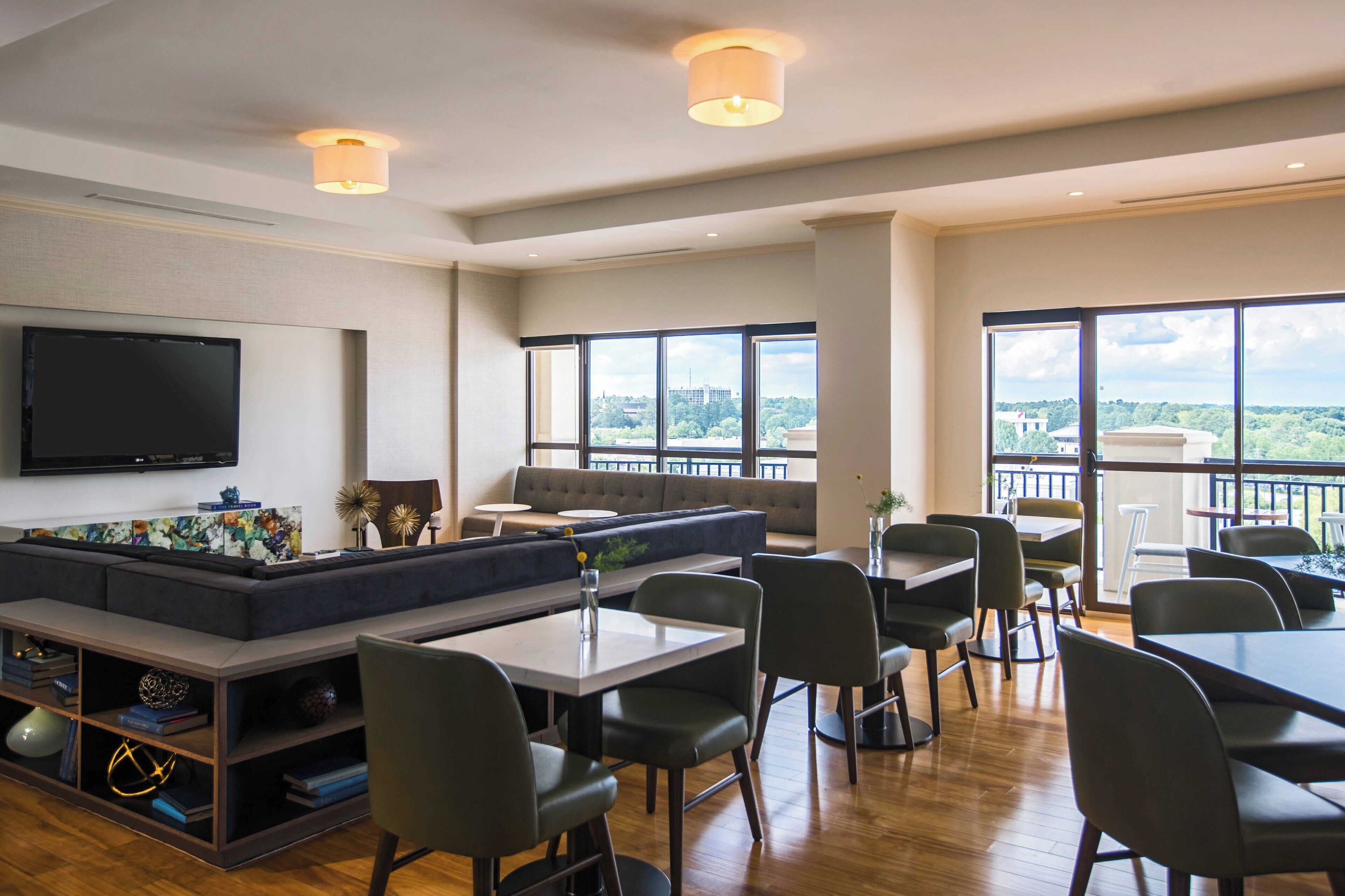 A modern dining area with a long table, multiple chairs, a sofa, and a television mounted on the wall.