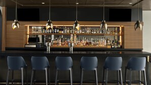 A bar area with a counter, bar stools, and a variety of bottles. - Renaissance Raleigh North Hills Hotel (Raleigh)