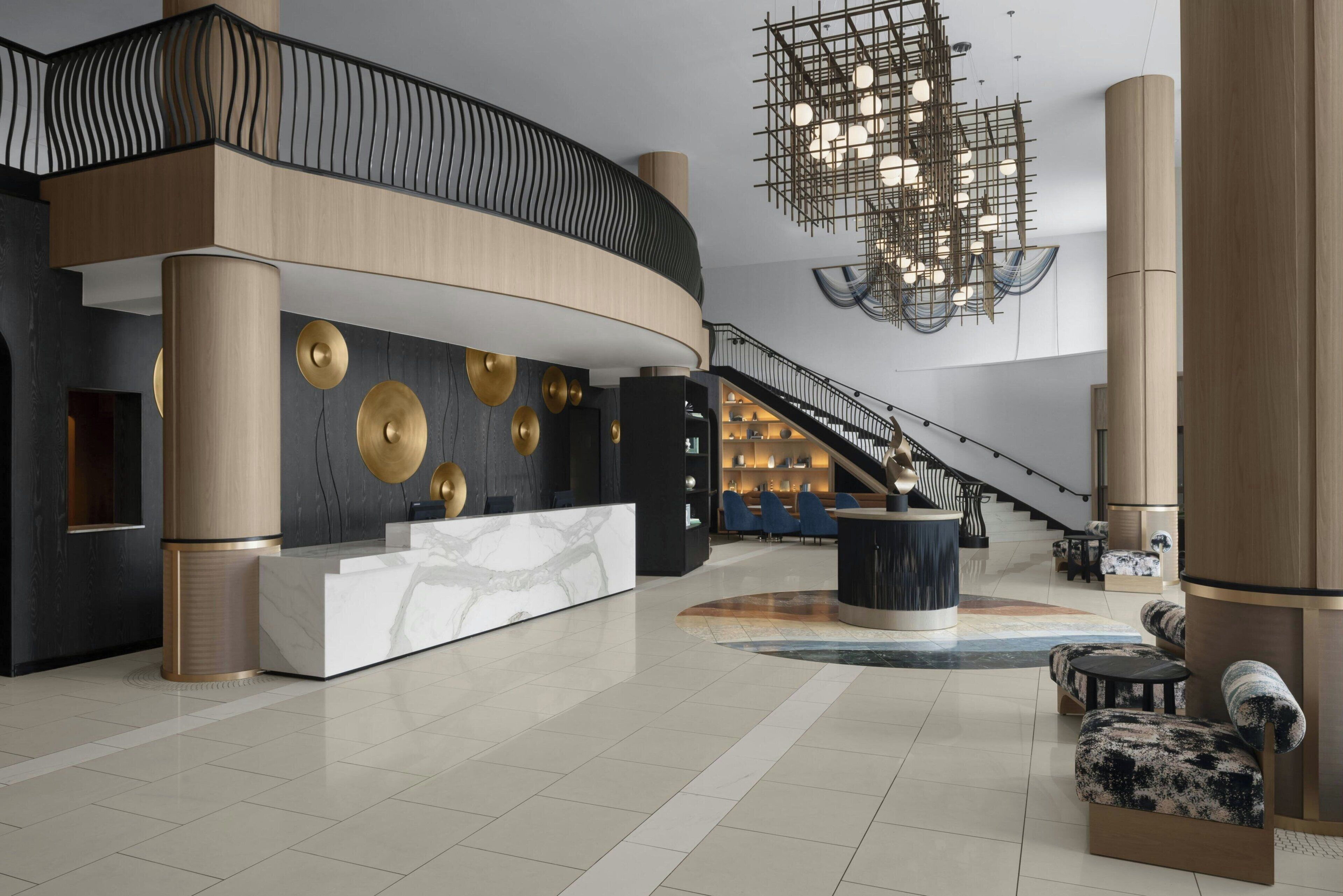 A spacious lobby with a curved reception desk, a staircase, and a modern chandelier.
