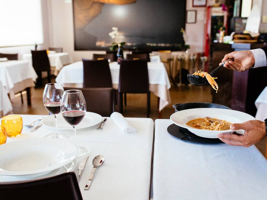 Ein Restaurant mit gedeckten Tischen, Weingläsern und einer Person, die Speisen serviert.