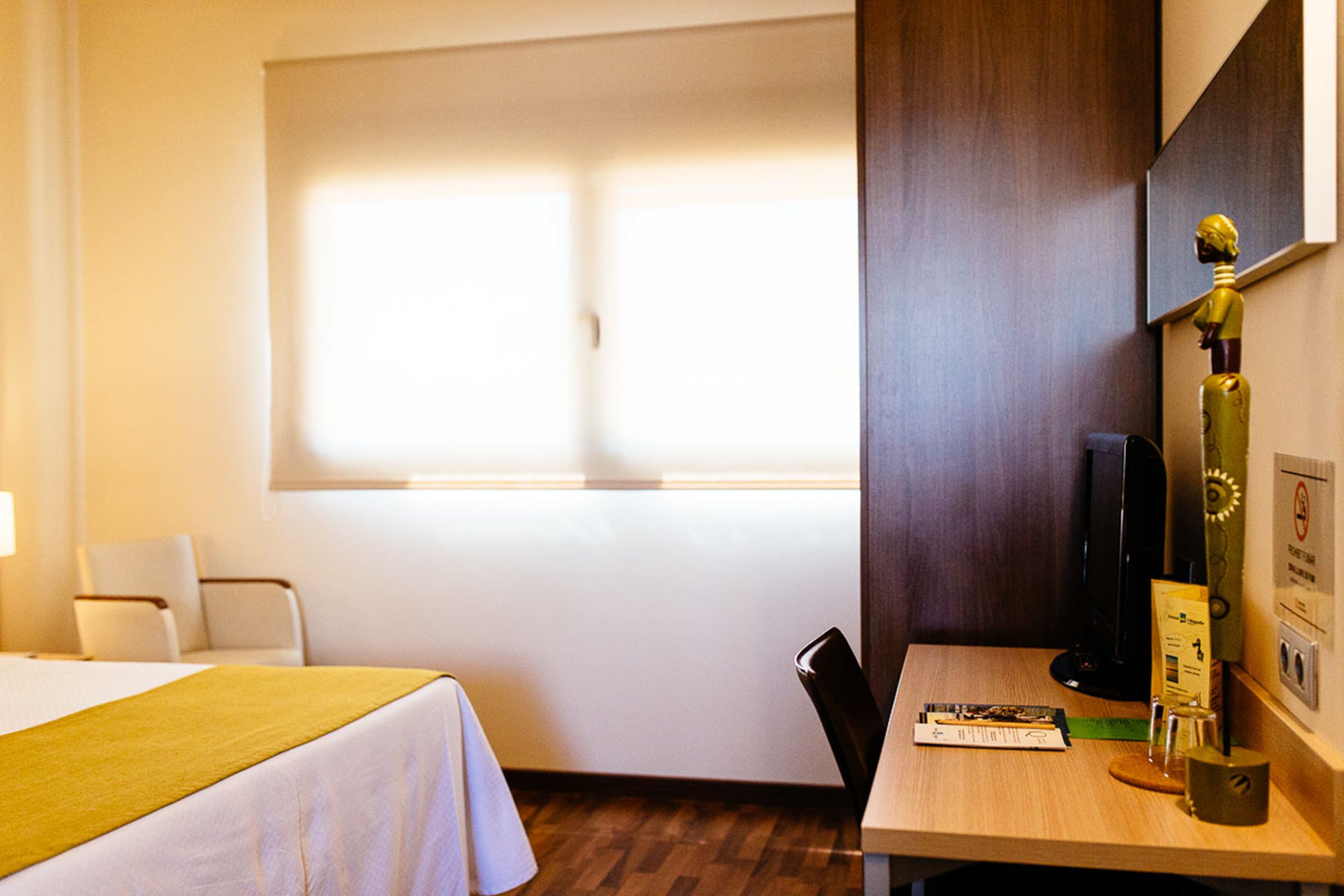 A hotel room with a bed, a desk, a chair, a window, and a wall-mounted TV.