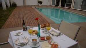 A dining table set for breakfast with croissants, juice, and coffee, near a swimming pool. - Hotel L'Algadir del Delta (Amposta)
