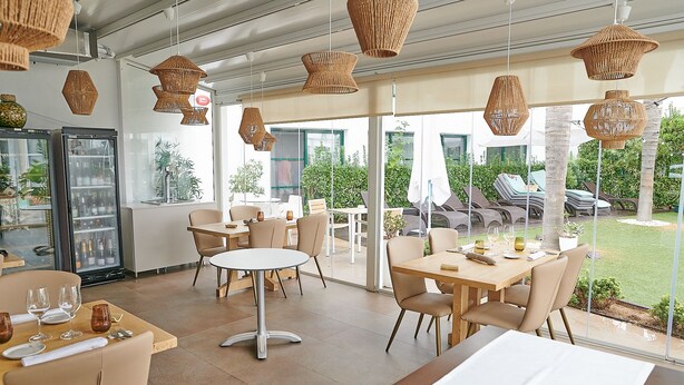A restaurant with tables and chairs, hanging wicker chandeliers, and a view of the outdoor seating area. - Hotel L'Algadir del Delta (Amposta)