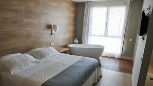 A modern bedroom with a large bed, a freestanding bathtub, and a large window with curtains. - Hotel L'Algadir del Delta (Amposta)