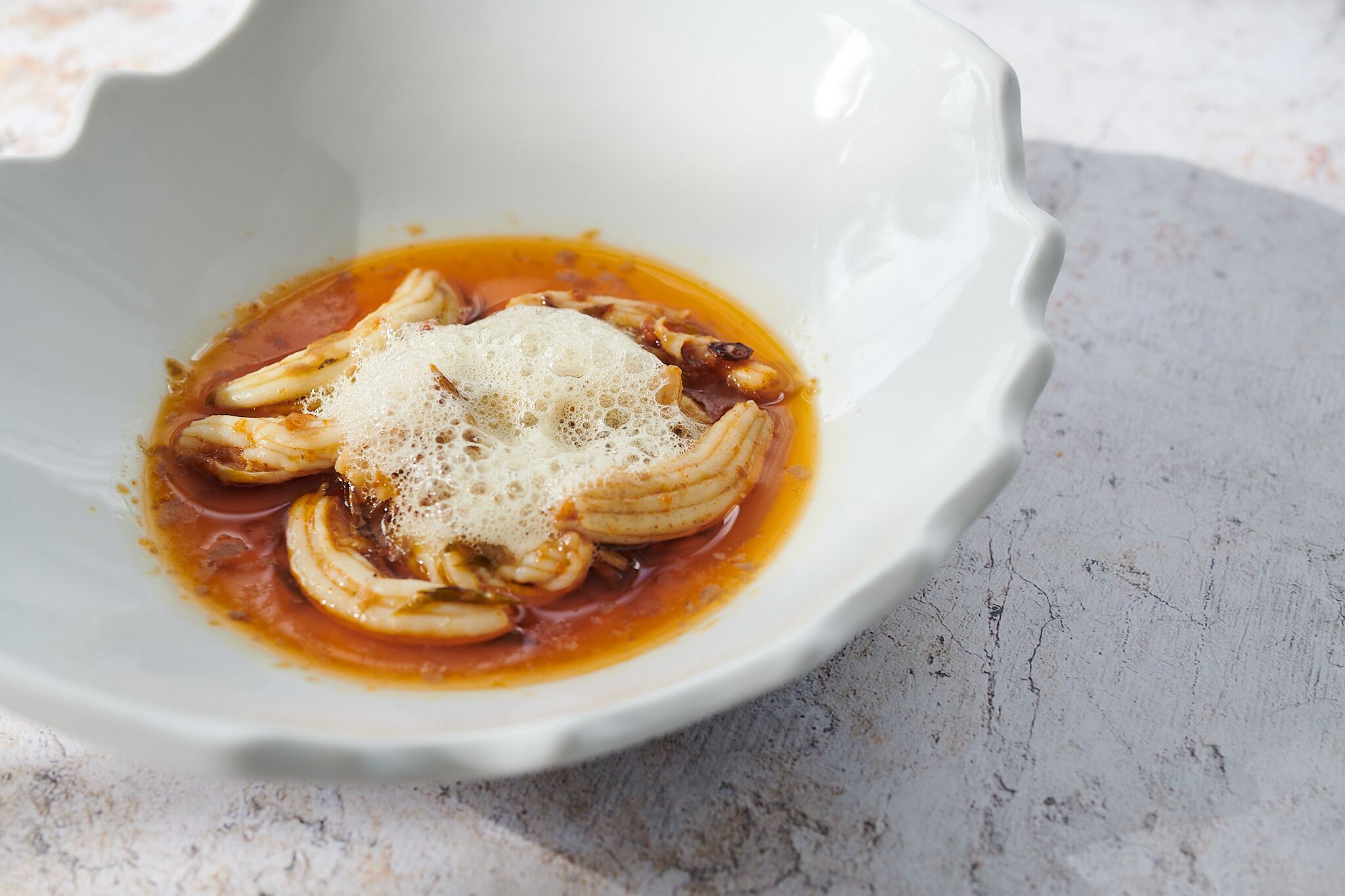 A white bowl with a sauce and sliced onions on a textured surface.
