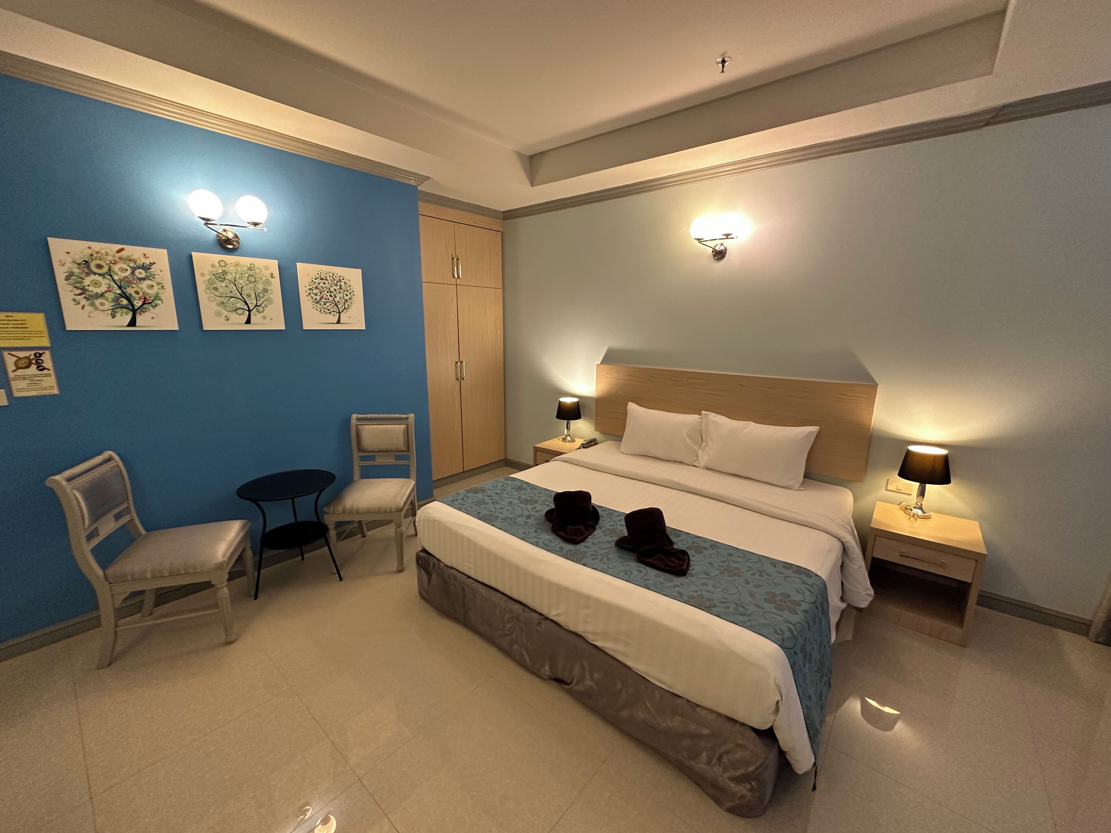 A hotel room with a bed, two bedside tables, a chair, a desk, and a wardrobe.