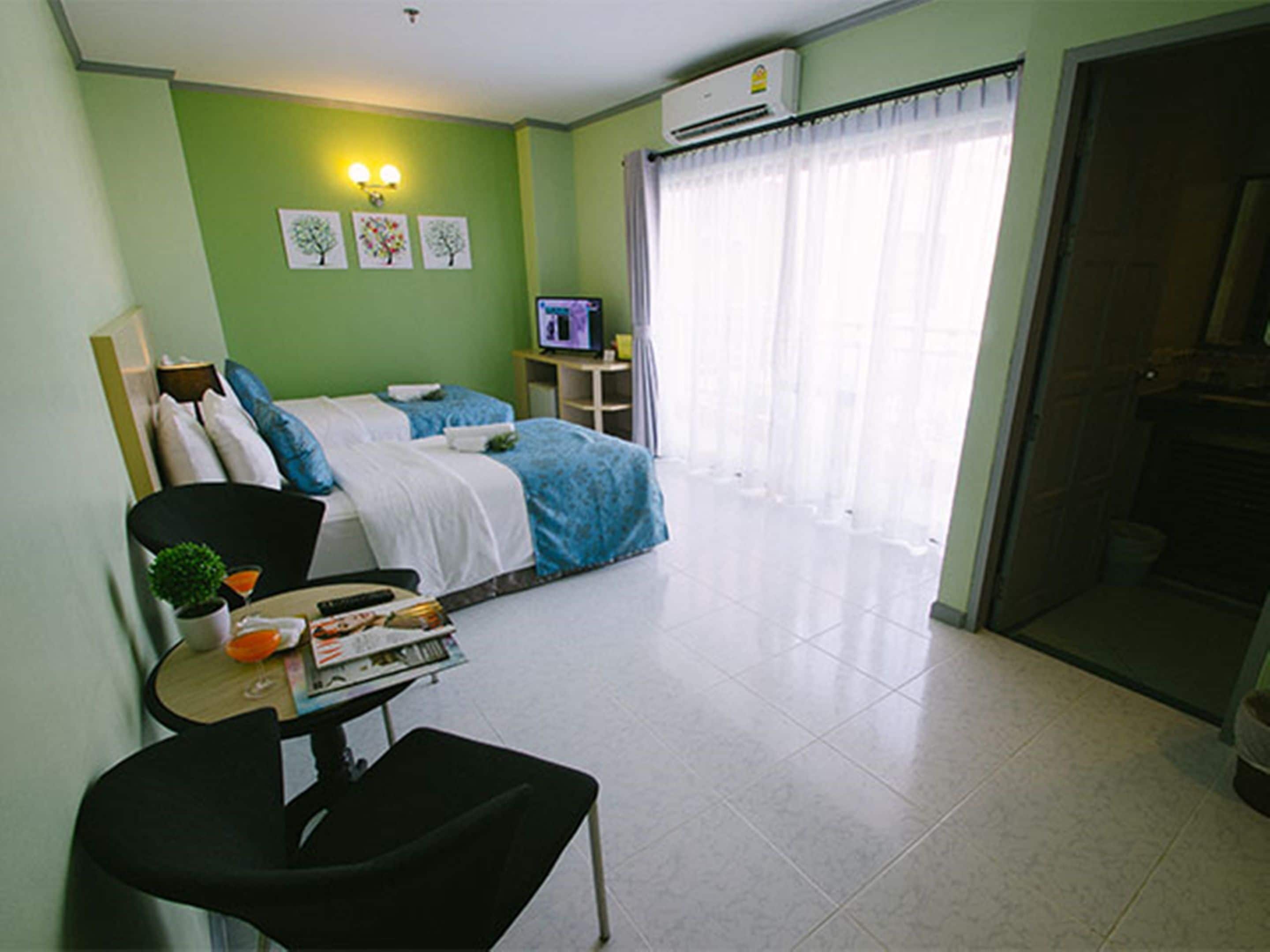 A hotel room with a bed, a desk with a chair, a television, and a window with curtains.
