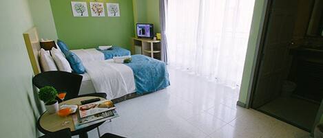 A hotel room with a bed, a desk with a chair, a television, and a window with curtains.