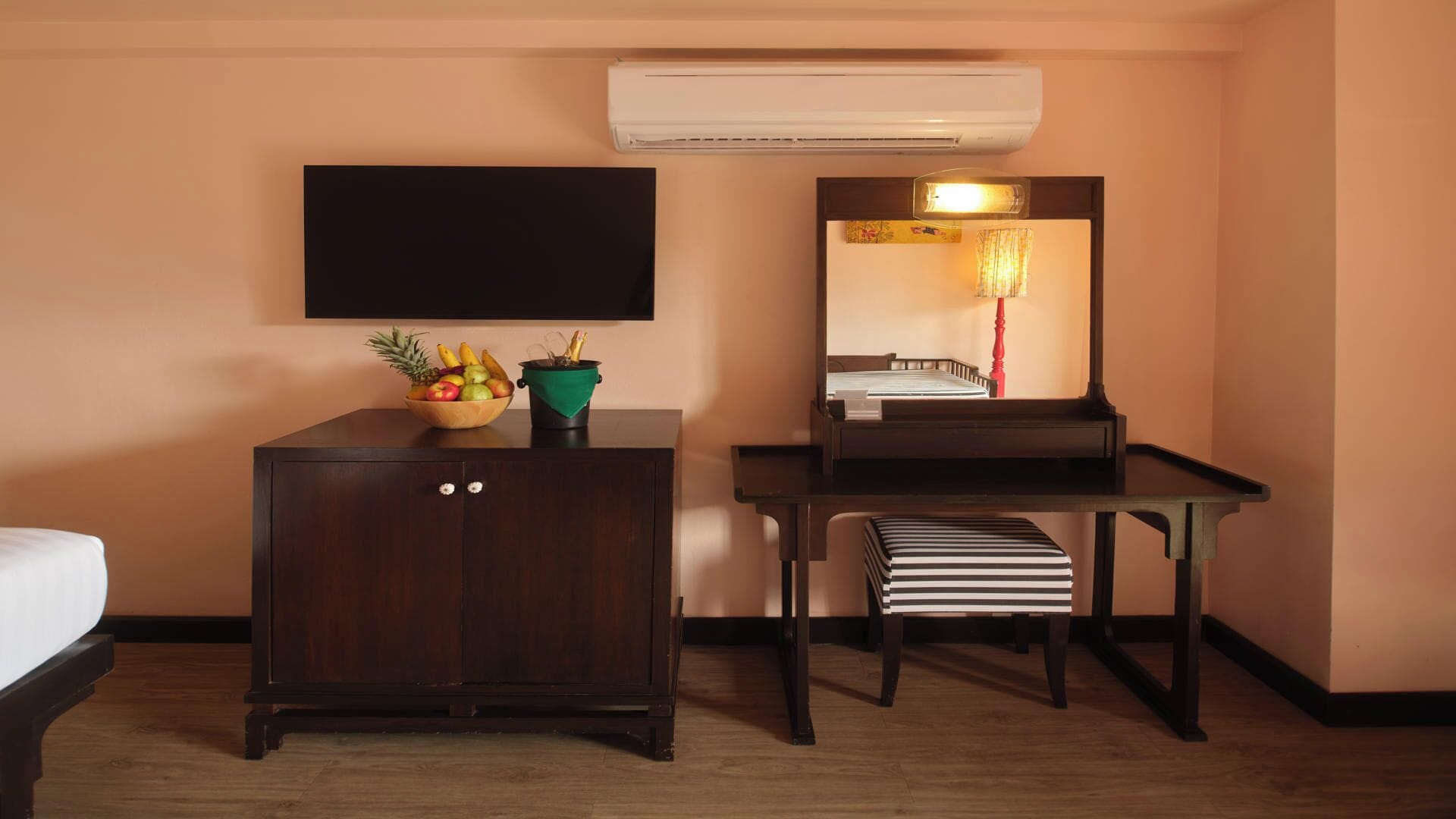 Habitación de hotel con un armario de madera, un taburete pequeño, un televisor de pantalla plana y un espejo.