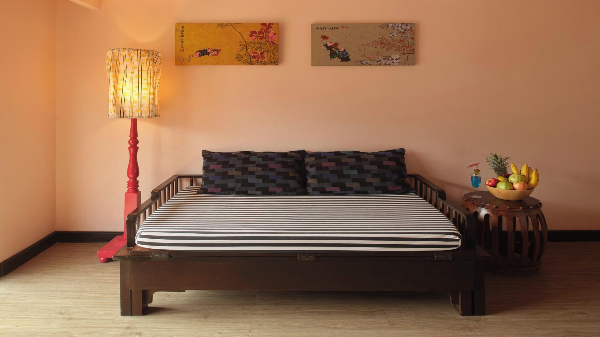 Un dormitorio con cama, mesita de noche, lámpara y dos obras de arte en las paredes.