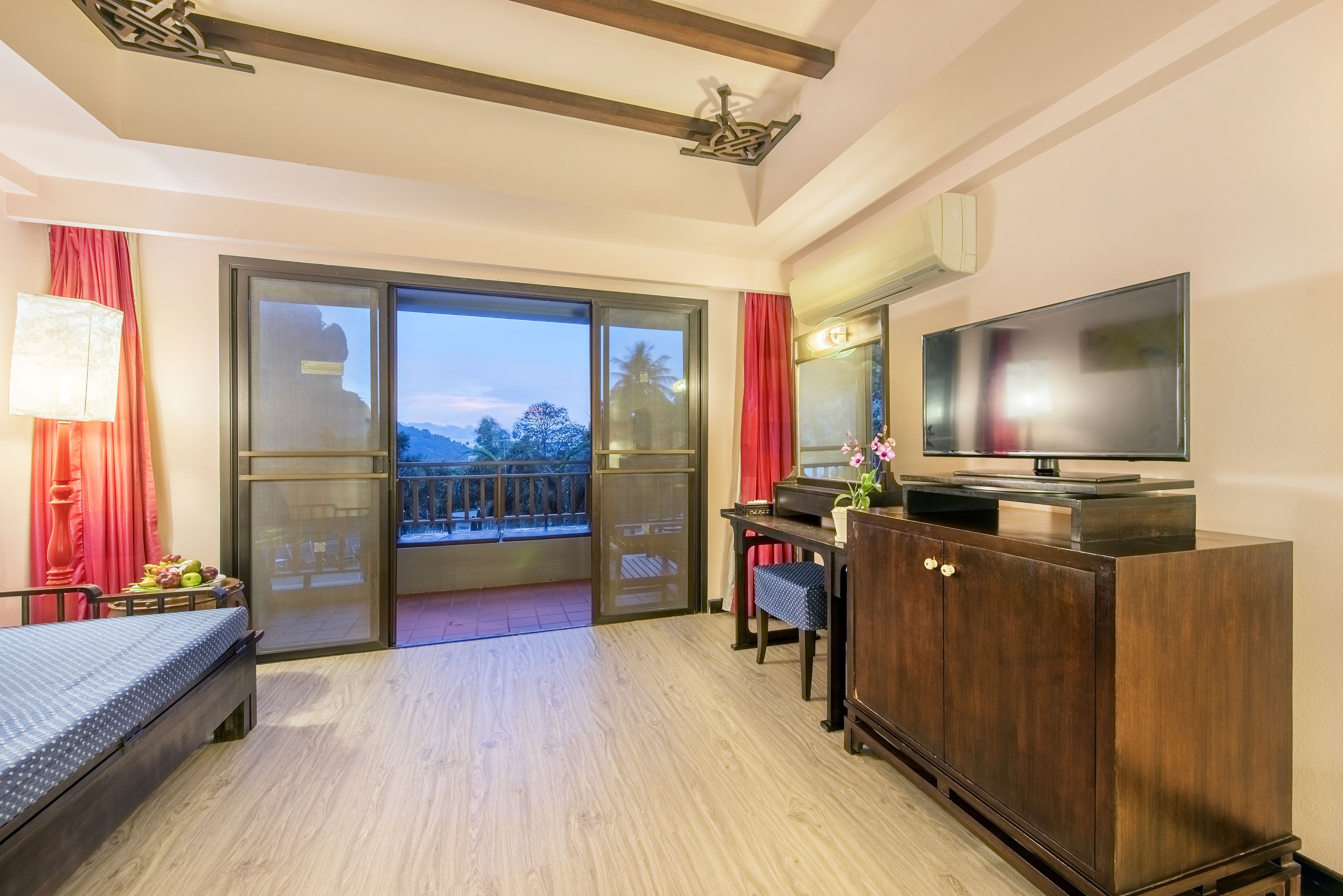 A hotel room with a bed, a desk, a TV, and a balcony with a view of the mountains.
