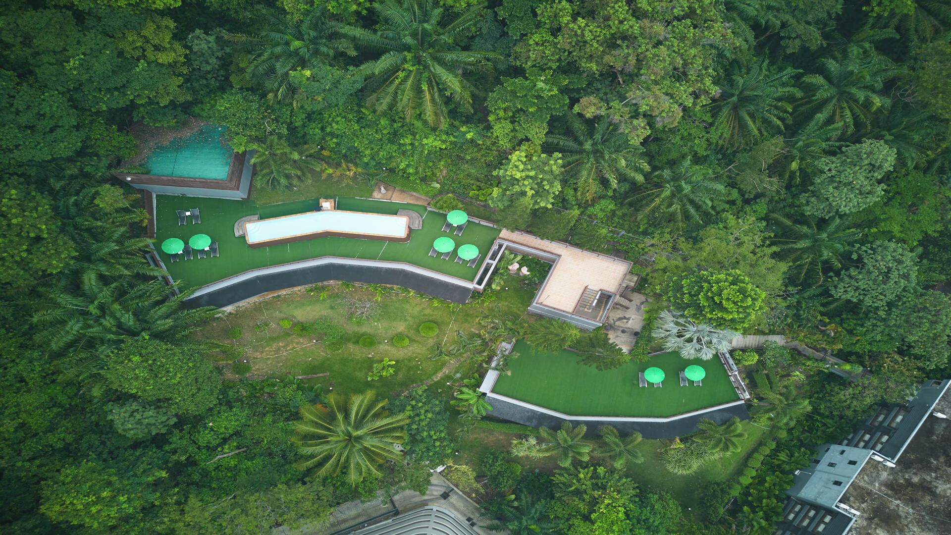 An aerial view of a resort with a swimming pool, lounge areas, and a small building.