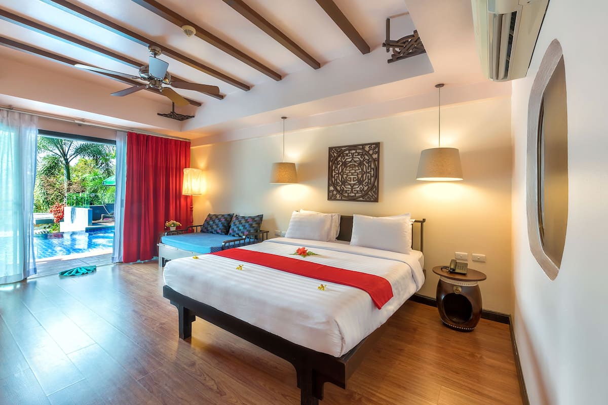 A spacious bedroom with a large bed, a ceiling fan, a view of a swimming pool, and a small table with a phone.
