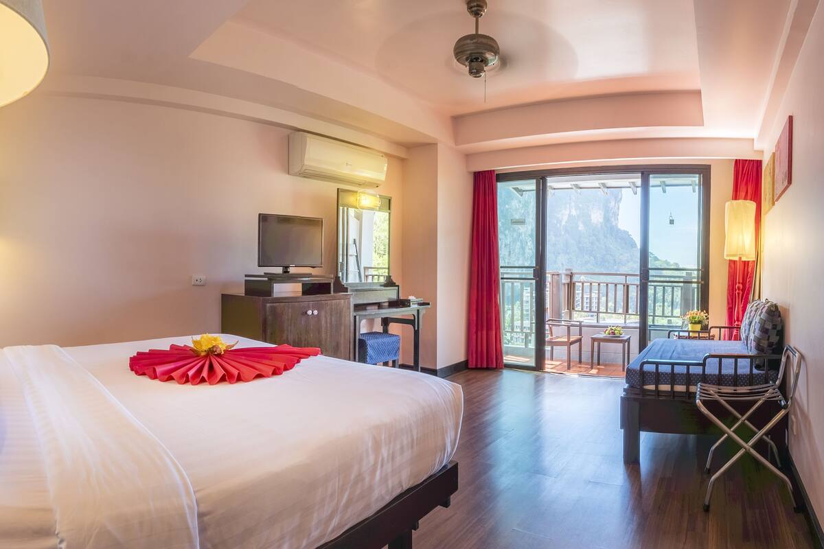 A hotel room with a bed, a desk, a TV, and a balcony with a view.