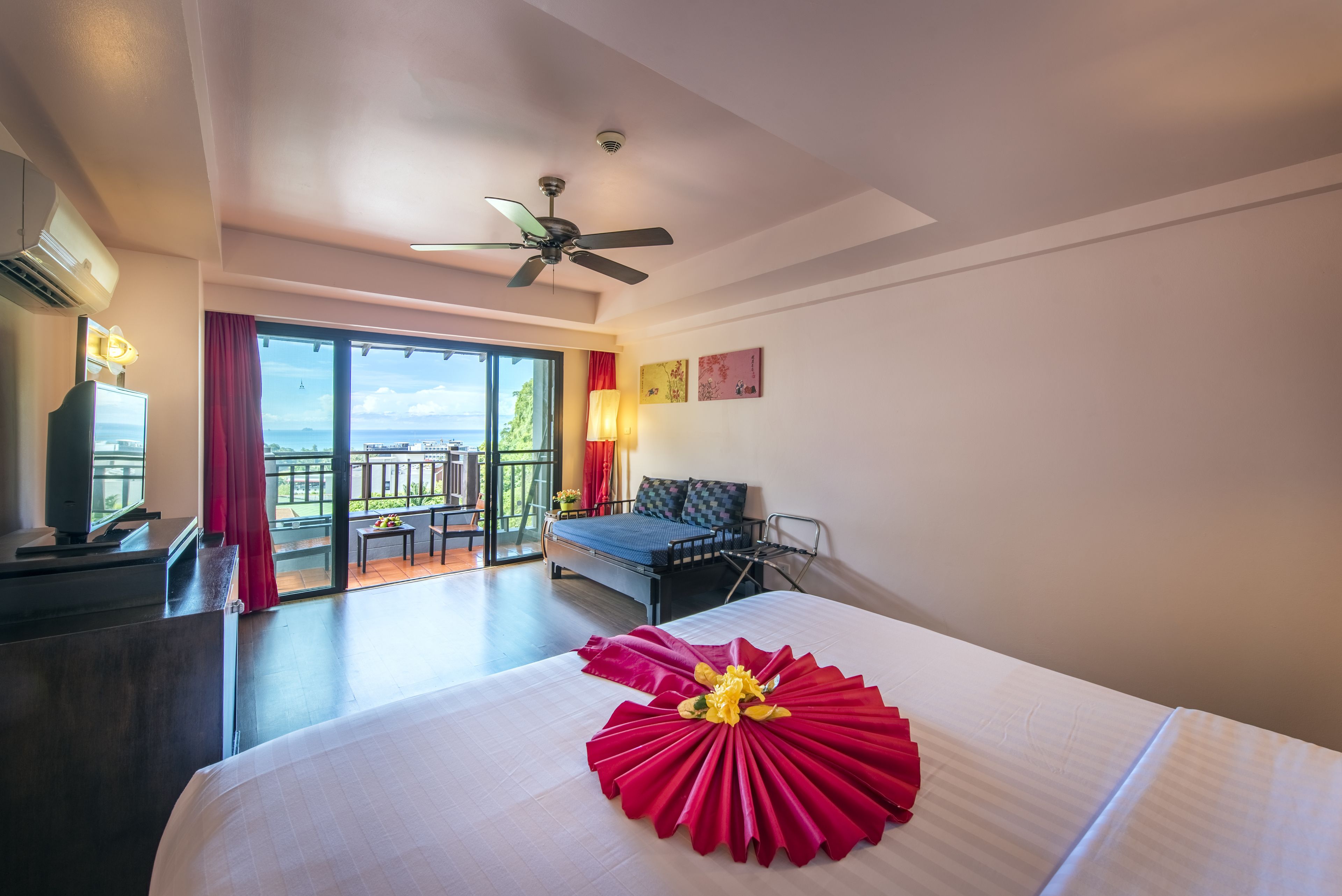 Habitación de hotel con cama, escritorio, silla, balcón con vistas y ventilador de techo.