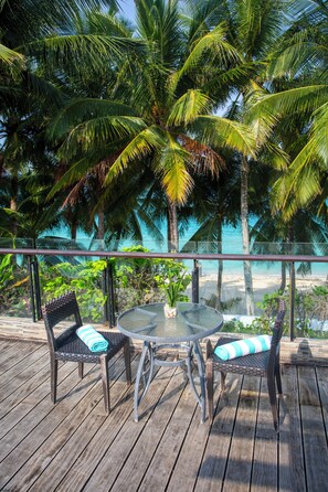 A wooden deck with two wicker chairs and a glass table, overlooking a beach with palm trees. - Crown Regency Beach Resort (Boracay Island)