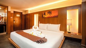 Habitación de hotel con una cama bien tendida, un cuadro de palmeras, una mesita de noche con una lámpara y una puerta de madera.