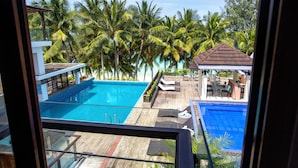 Vista de una piscina con sillas de descanso y un pabellón, rodeado de palmeras.