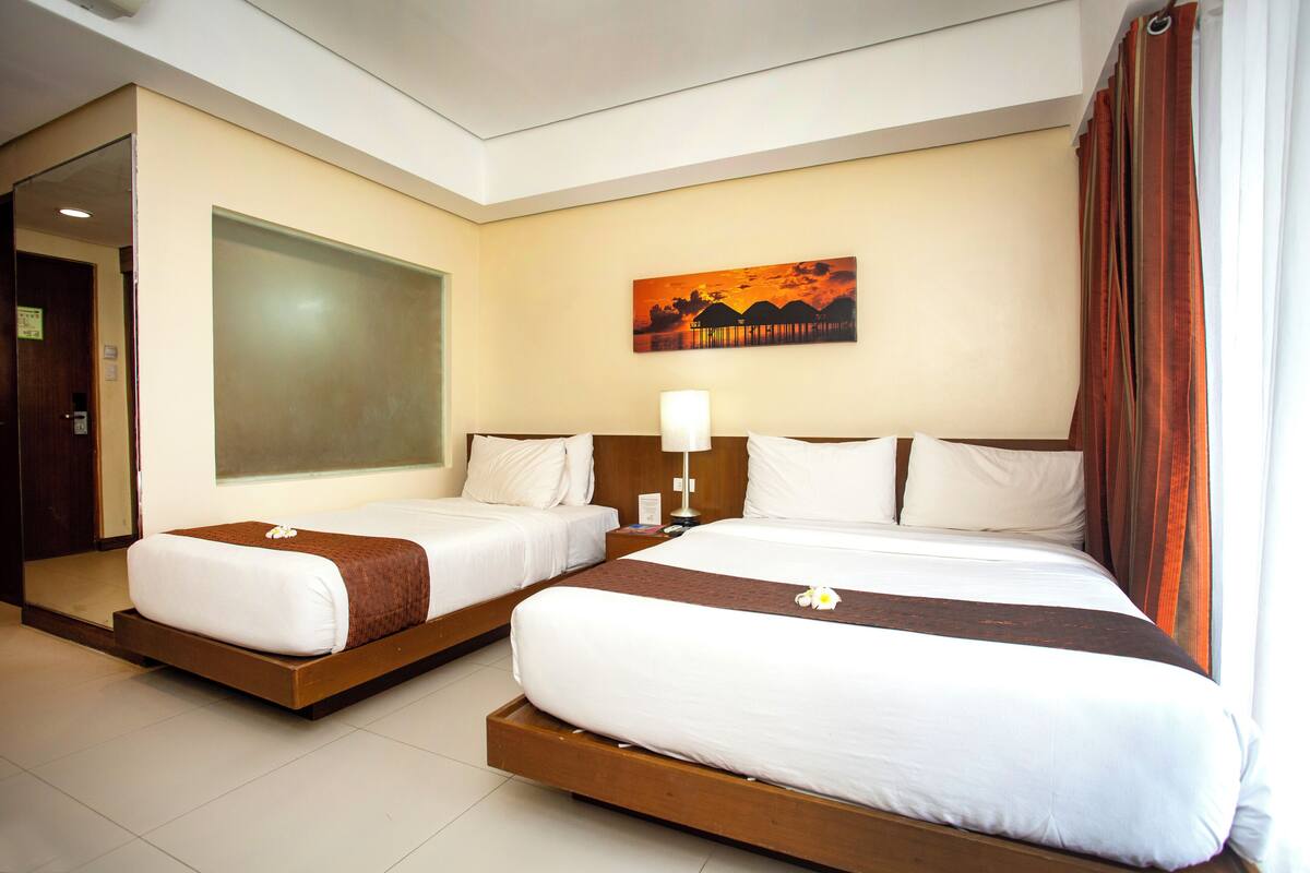A hotel room with two beds, a large window, a painting on the wall, and a door.