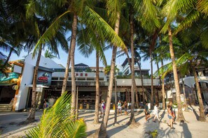 A beachfront area with palm trees, a building with a sign, and people walking. - Crown Regency Beach Resort (Boracay Island)
