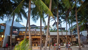 Zona de playa con palmeras, un restaurante y un edificio con un letrero.