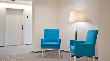 Un hall de hotel con dos sillones azules, una lámpara de pie y una alfombra estampada.