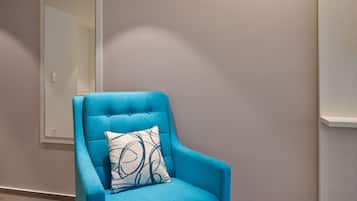 Un fauteuil bleu avec un coussin à motifs, dans une pièce dotée d’un grand miroir, d’un sol recouvert d’une moquette et d’un éclairage encastré au plafond.