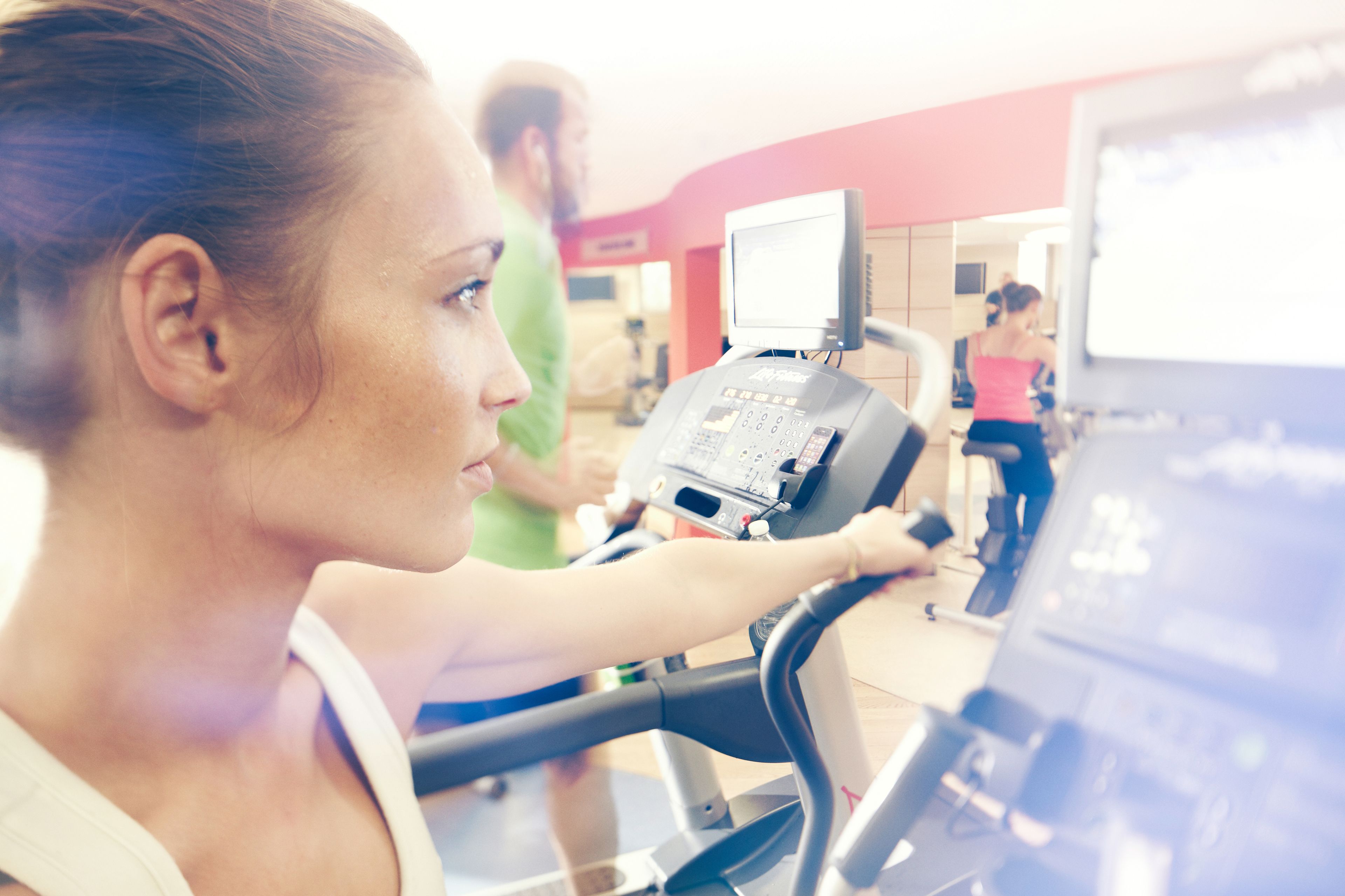 A woman using an exercise machine in a gym with a digital display and a mirror.