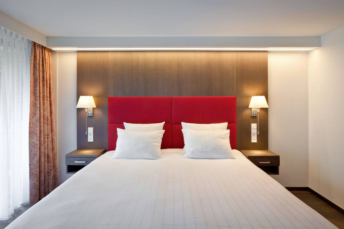 Una habitación de hotel con una cama grande, dos mesitas de noche y un cabecero rojo.