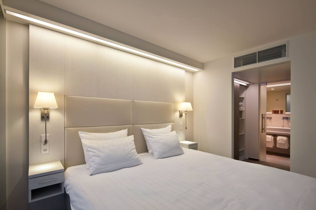 Una habitación de hotel con una cama grande, dos mesitas de noche y un vestidor.