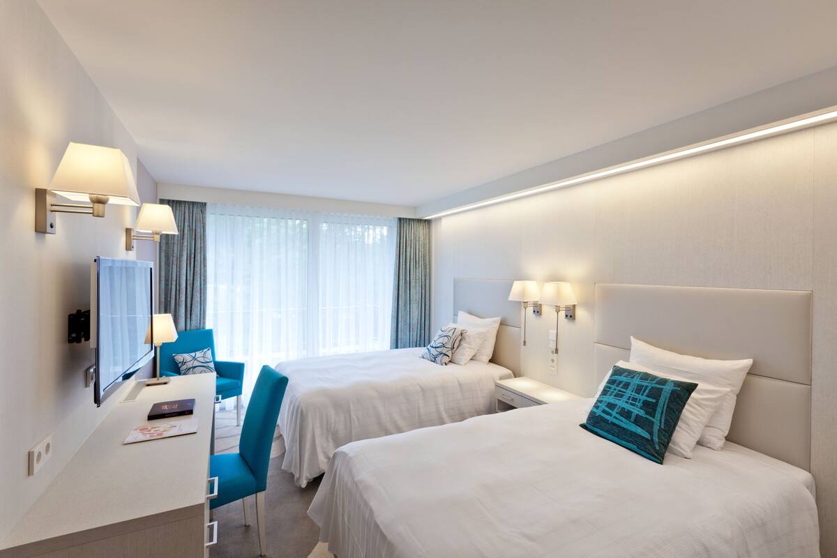 Habitación de hotel con dos camas, un escritorio, una silla y una ventana con cortinas.