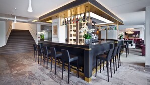 A modern kitchen with a central island, bar area with stools, and a staircase.