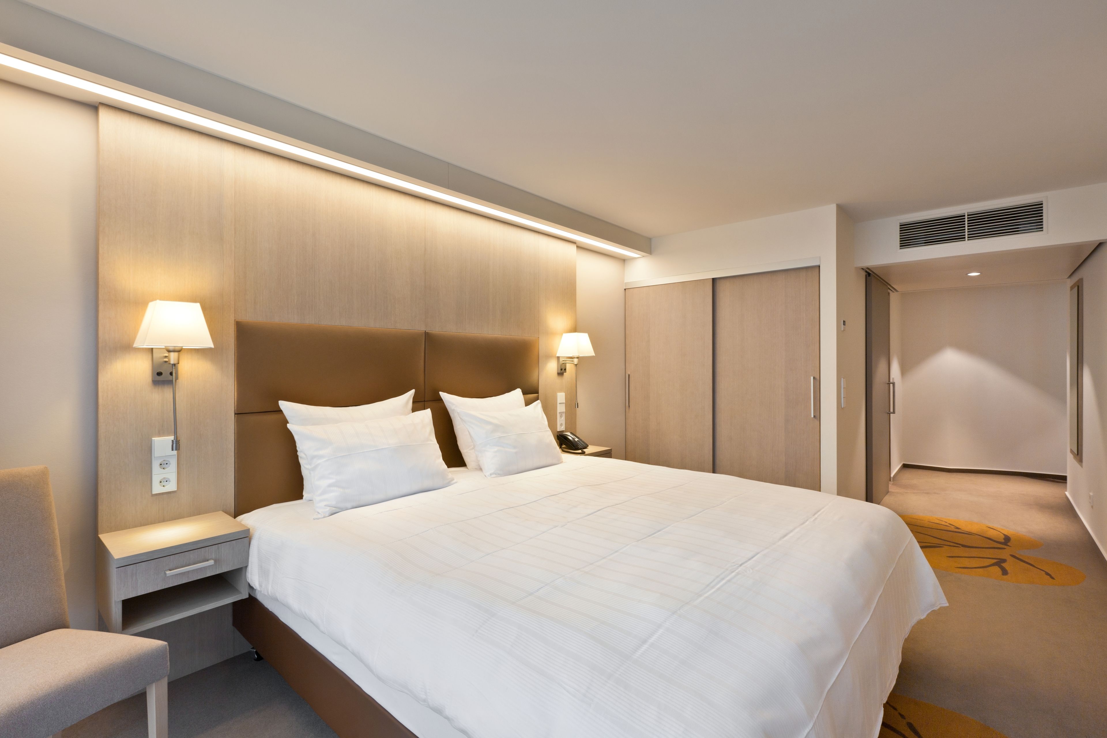 Camera d'albergo con un letto grande, comodini con lampade, un armadio e un tappeto con motivo alberato.