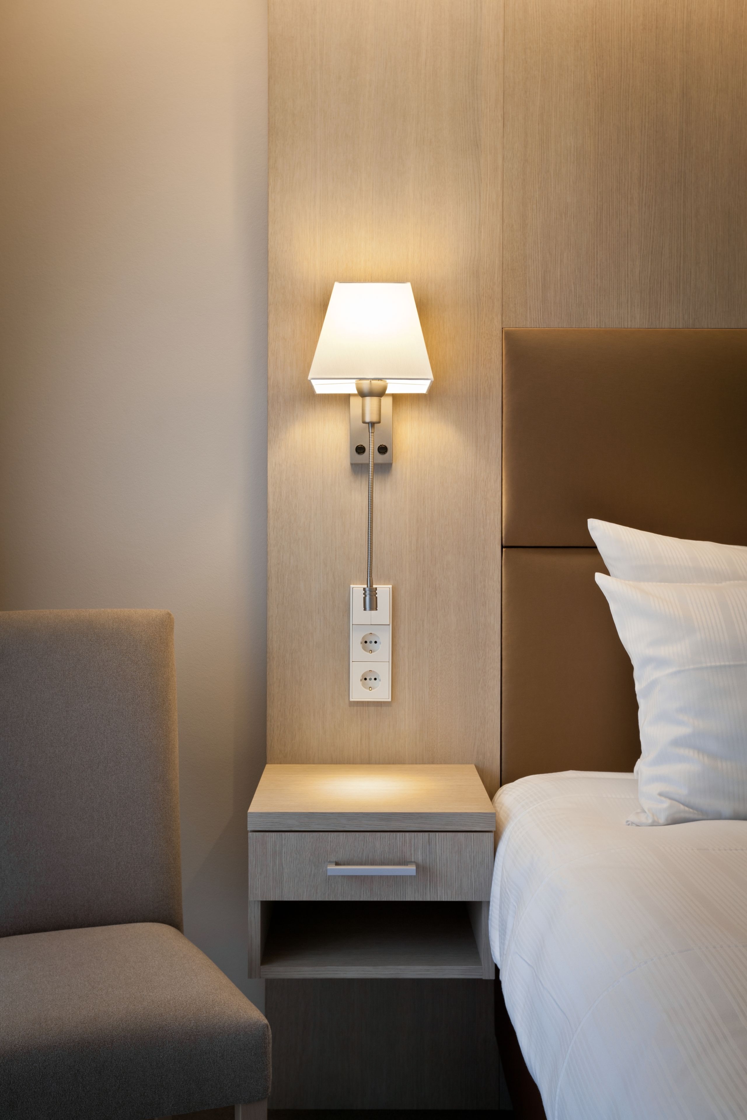 Une chambre d’hôtel avec une table de chevet, une lampe, une chaise et un lit avec du linge de lit blanc.