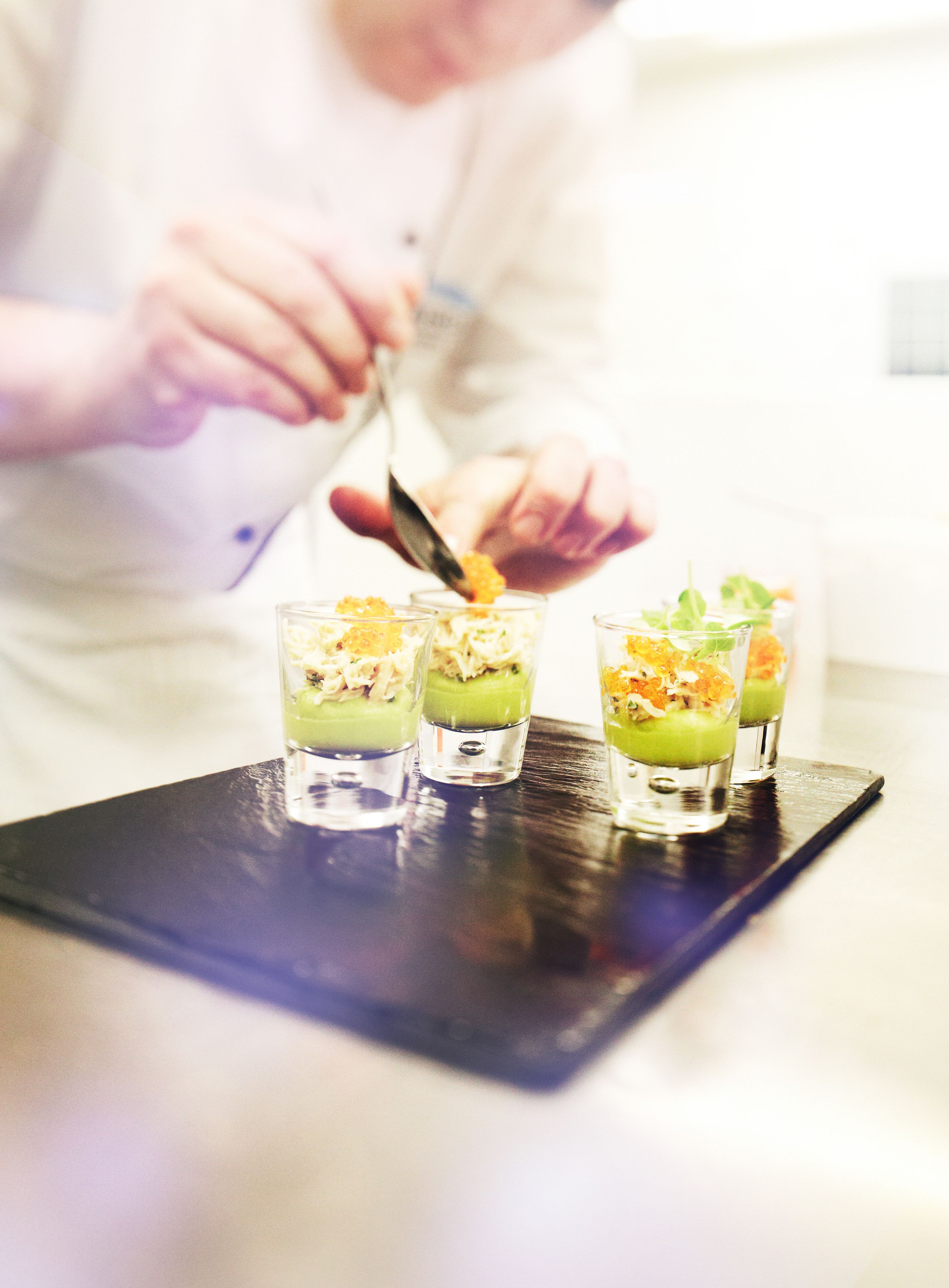 A chef preparing a dish with three glasses on a black tray.