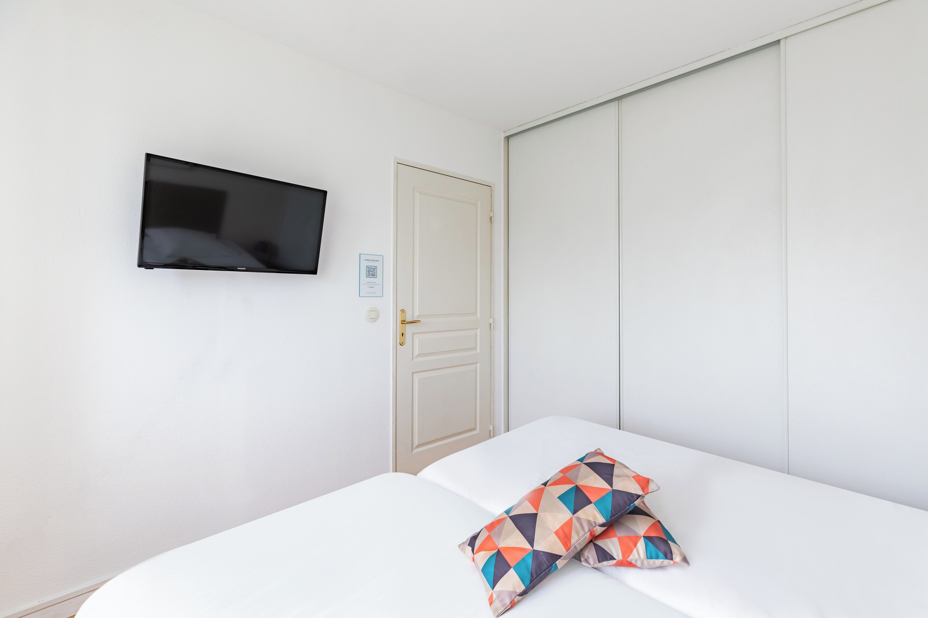 A room with a bed, a television mounted on the wall, and a door.