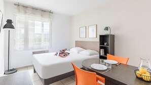 A hotel room with a bed, a dining table with chairs, a bookshelf, and a window with curtains. - Appart'City Classic Thonon les bains (Thonon-les-Bains)