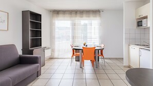 A modern living room with a sofa, dining table, chairs, and a kitchen area with a microwave. - Appart'City Classic Thonon les bains (Thonon-les-Bains)