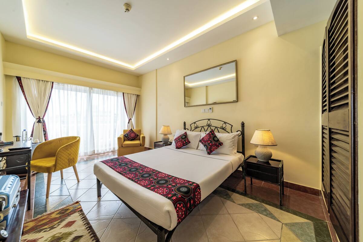 A hotel room with a bed, bedside tables, a desk, a chair, and a window with curtains.