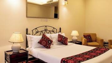 Habitación de hotel con una cama, dos mesitas de noche, una silla, un espejo y dos lámparas de pared.
