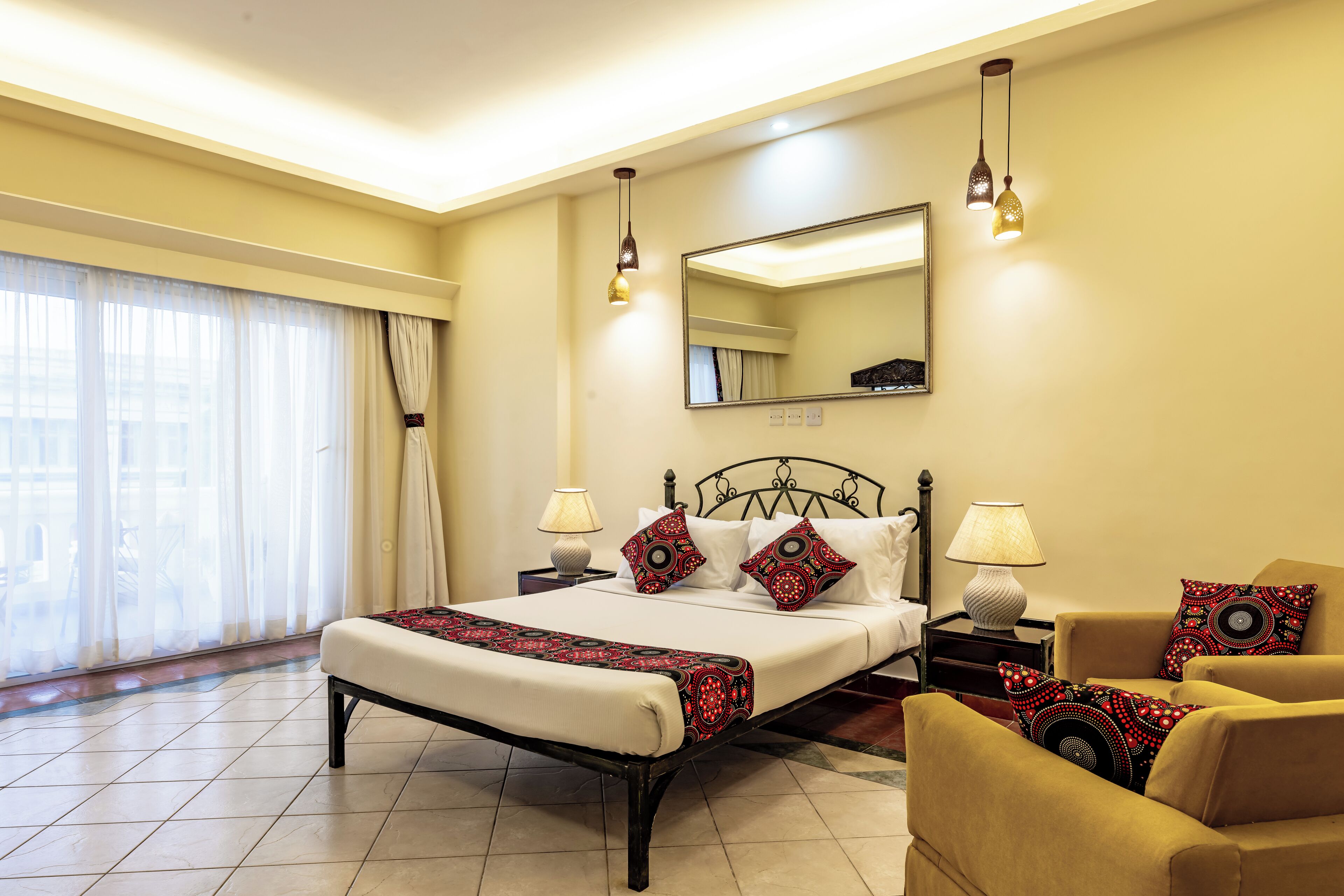 Quarto de hotel com cama, mesas de cabeceira, uma cadeira, uma janela grande com cortinas e um espelho na parede.