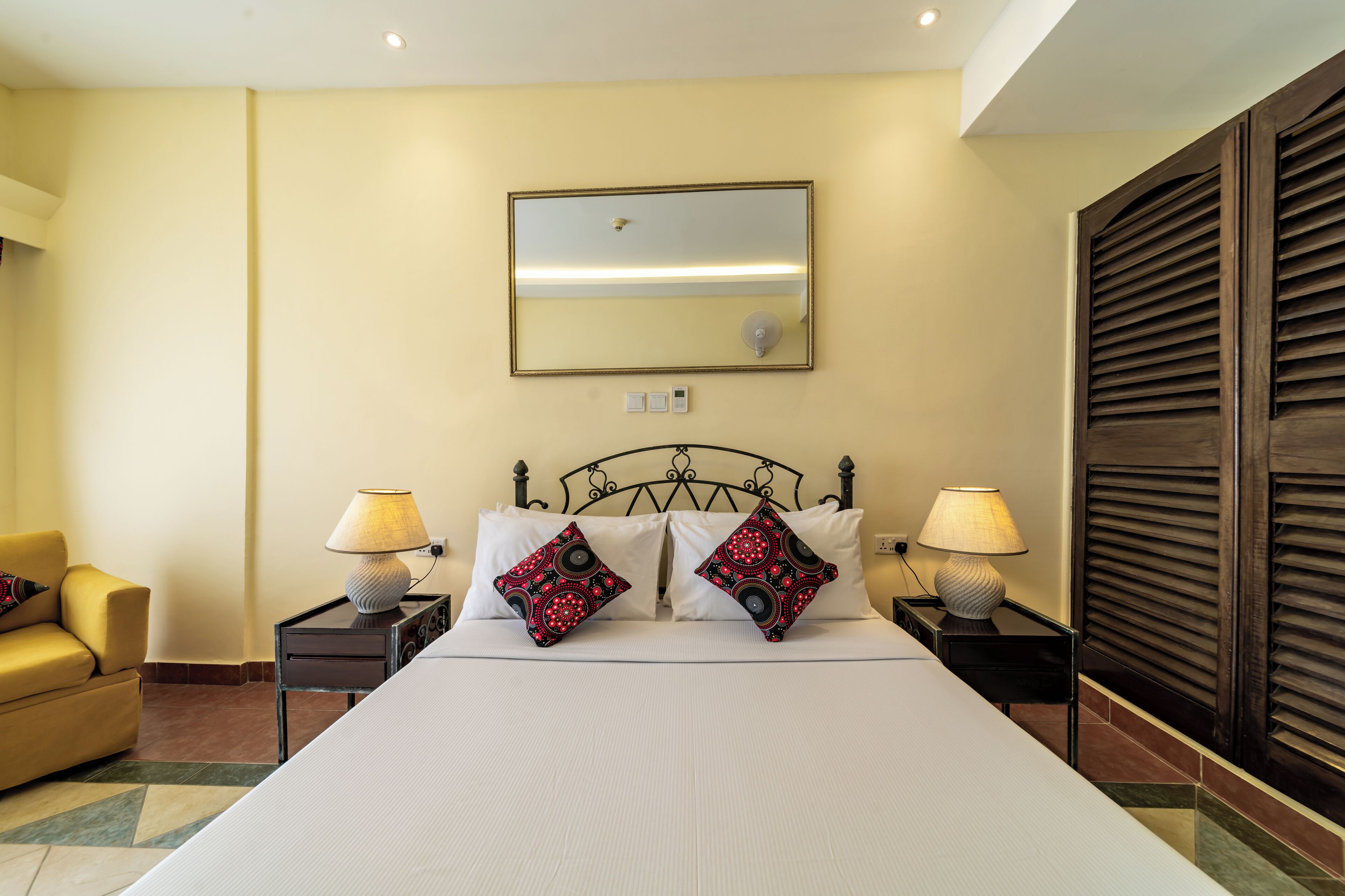 Een hotelkamer met een groot bed, twee nachtkastjes met lampen, een stoel en een spiegel aan de muur.