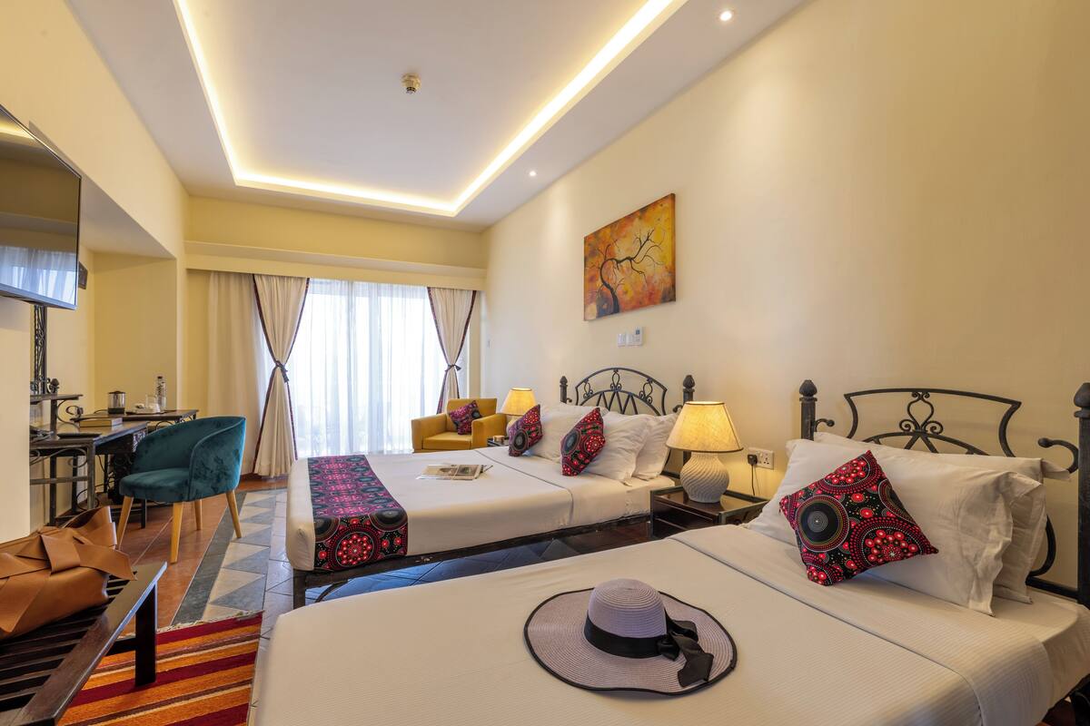A hotel room with two beds, a desk, a chair, and a painting on the wall.